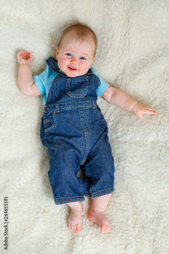 Adorable five month old baby girl in denim dungarees lying on bed