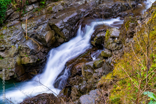 Fantastic landscape view of waterfall flowing around rocks with greens and stones in long exposure.