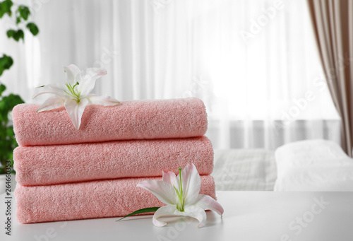 Stack of fresh towels with flowers on table in bedroom. Space for text