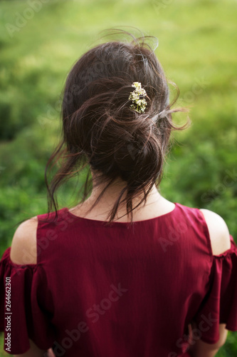 Back view of young romantic woman in red dress. Windy day, white flower in hair.