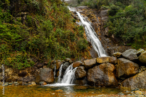 Beautiful landscape view of waterfall flowing around rocks with greens and stones.