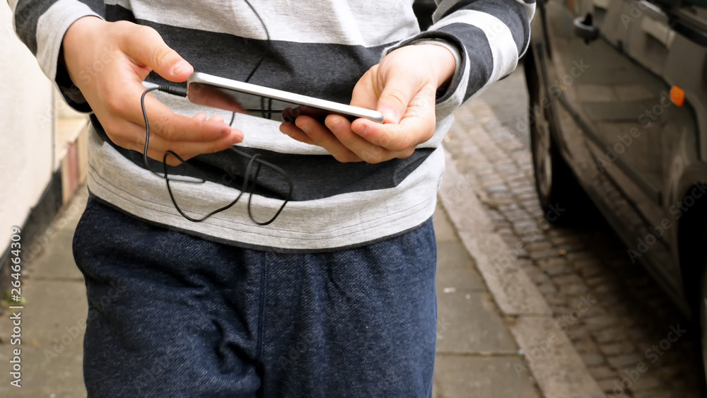 teen hands with smart phone walking and listening or talking on british street. teenager and social media concept