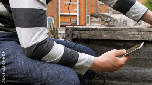 teen boy with smart phone listening or talking while sitting in british backyard garden. teenager and social media concept