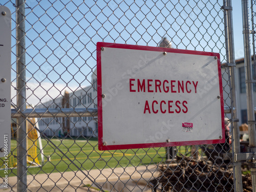 Emergency access sign posted on chain-link fence guarding a school sports area