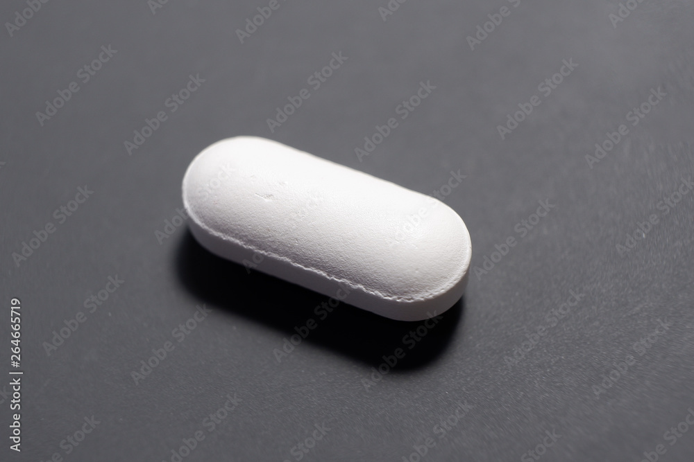 A pill resting on a dark matte background A pill resting on a dark matte background
