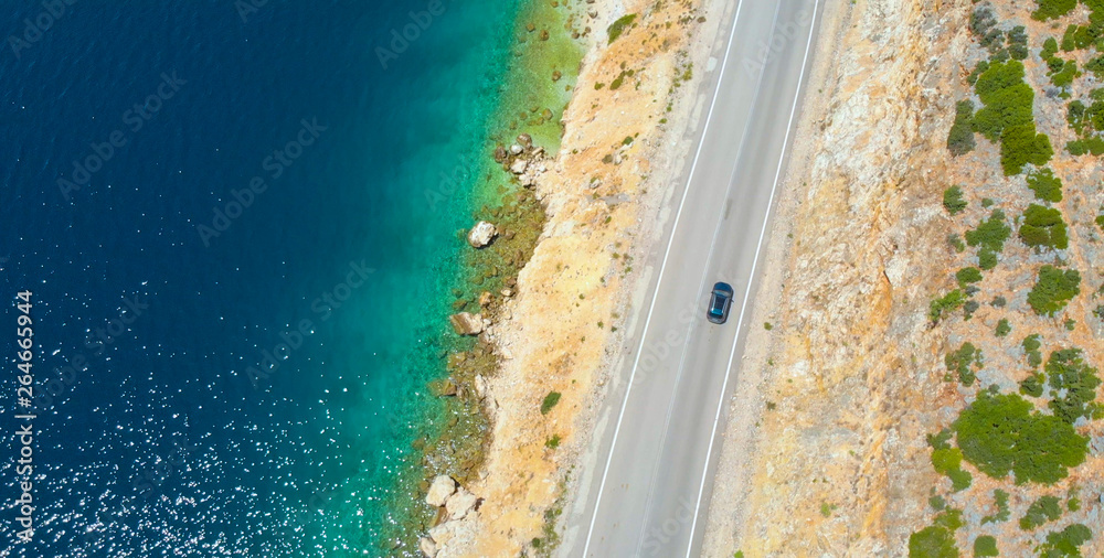 TOP DOWN: Car cruises down the empty road leading along beautiful rocky beach.
