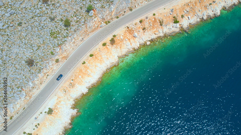 AERIAL: Tourist car cruises down the scenic coastal road running along the ocean