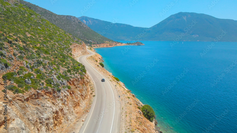 DRONE: Flying behind a car exploring the island by driving down a coastal road.