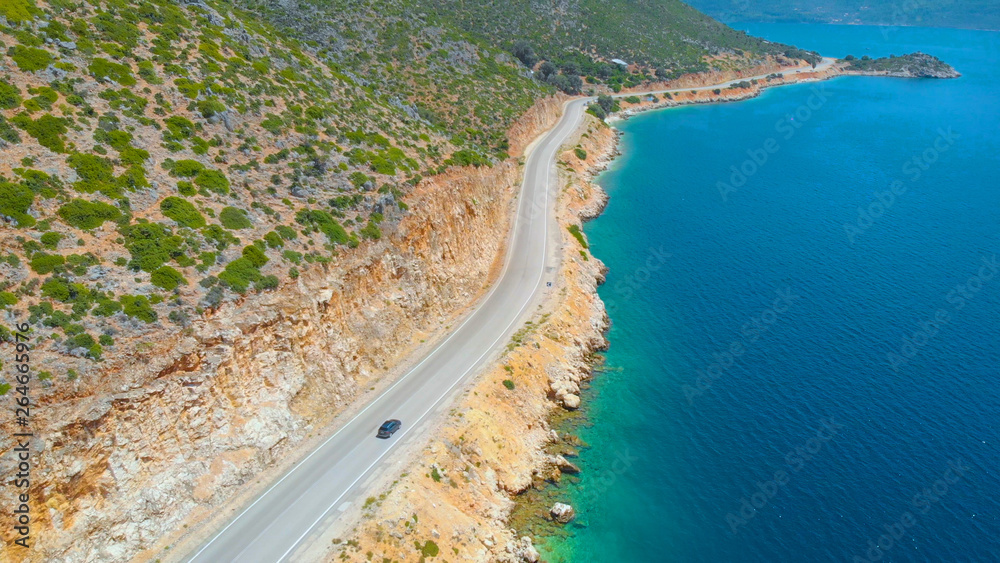 AERIAL: Flying over the emerald ocean as car cruises along the coastal road.