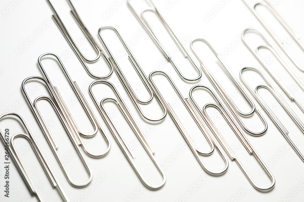 New office metal clips are on the bright surface. Long Clips are on the light in the form of a diagram. Selective focus.