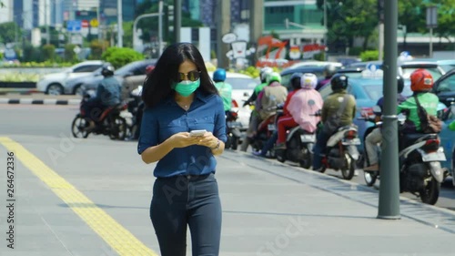 Wallpaper Mural JAKARTA, Indonesia - April 24, 2019: Air Pollution Concept. Young woman wearing a mask while walking on the sidewalk and using a mobile phone. Shot in 4k resolution Torontodigital.ca