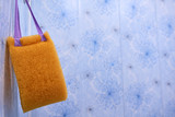 yellow washcloth with handles hung on a hook in the bathroom on a beautiful blue blurred background. accessories for the care of the body in the bathroom. clean healthy body concept. copy space