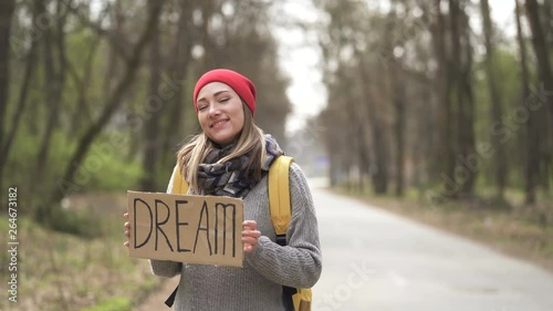 Waiting car. Young hitchhiking woman go on road with poster dream photo