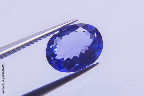 Big blue gemstone Placed on the wooden floor.blue sapphire oval stone in tweezer
