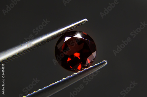 Red Garnet.Dark red gemstone.Beautiful round shape gem.stone in tweezers.Focus on the center of the image.The background is not smooth.