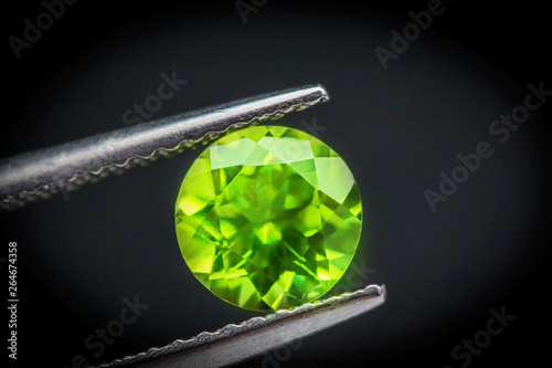 Peridot gemstone.Beautiful round shape gem.Natural Green Sapphire.stone in tweezers.Focus on the center of the image.The background is not smooth.