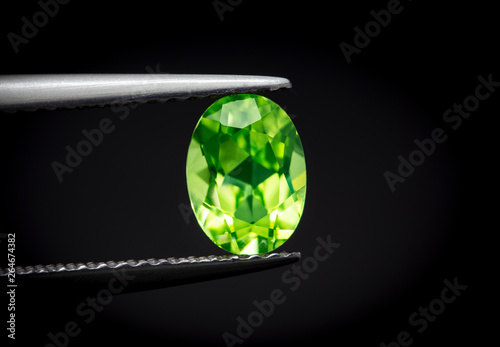 Natural Peridot Gems Stone oval cut beautiful.Holding a green stone by tweezers.
