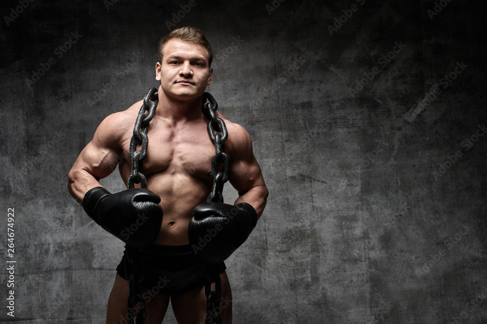 Obraz premium Muscular pumped man boxing in gloves on a black background. Sexy athlete with a huge chain around his neck