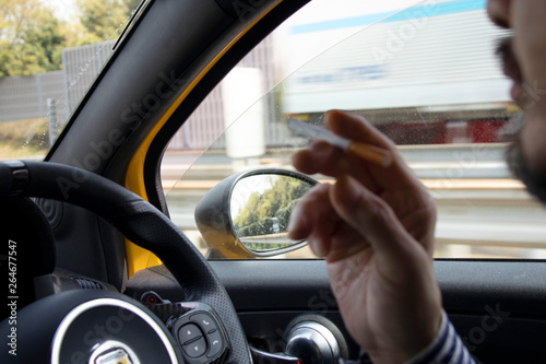 車を運転しながらタバコを吸う男性 © decoplus
