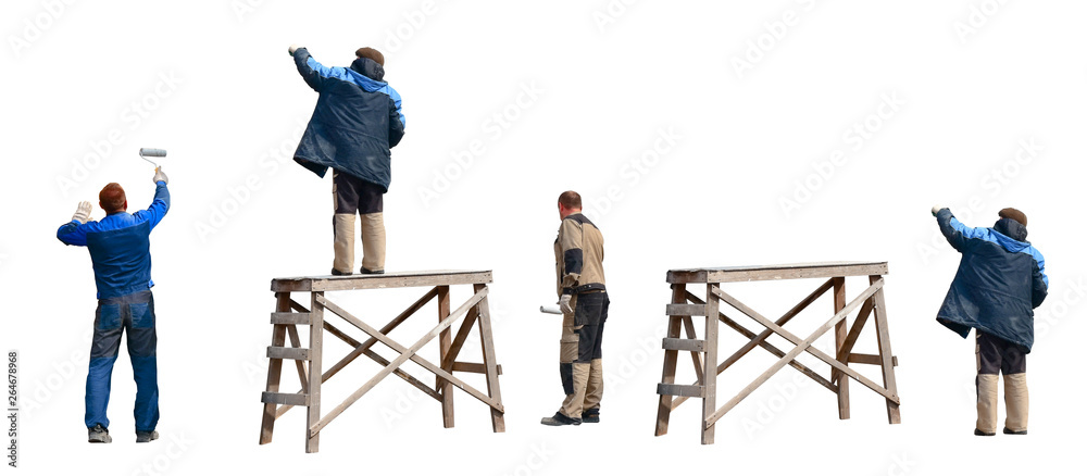 Three painters in overalls paint by hand an old wooden wall in gray
