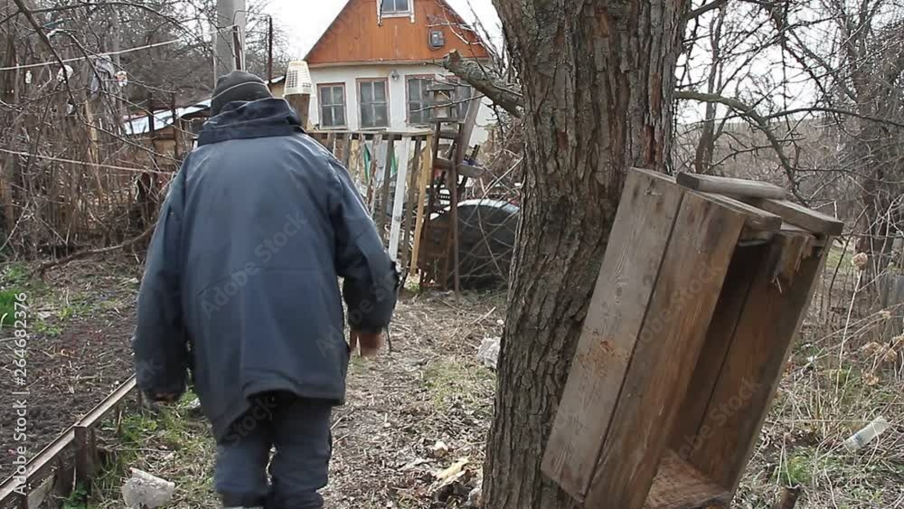 The poor old grandfather walks through the patch of land to the rickety gate and the old collapsed house. Life in an abandoned village. The poor old grandfather walks through the patch of land to the rickety gate and the old collapsed house. Life in an abandoned village.