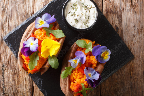 Delicious baked sweet potato with cream cheese decorated with edible flowers close-up on the table. horizontal top view from above