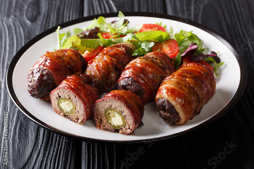 Traditional American Armadillo eggs stuffed with jalapeno and cheese wrapped in bacon served with salad close-up on a plate on the table. horizontal