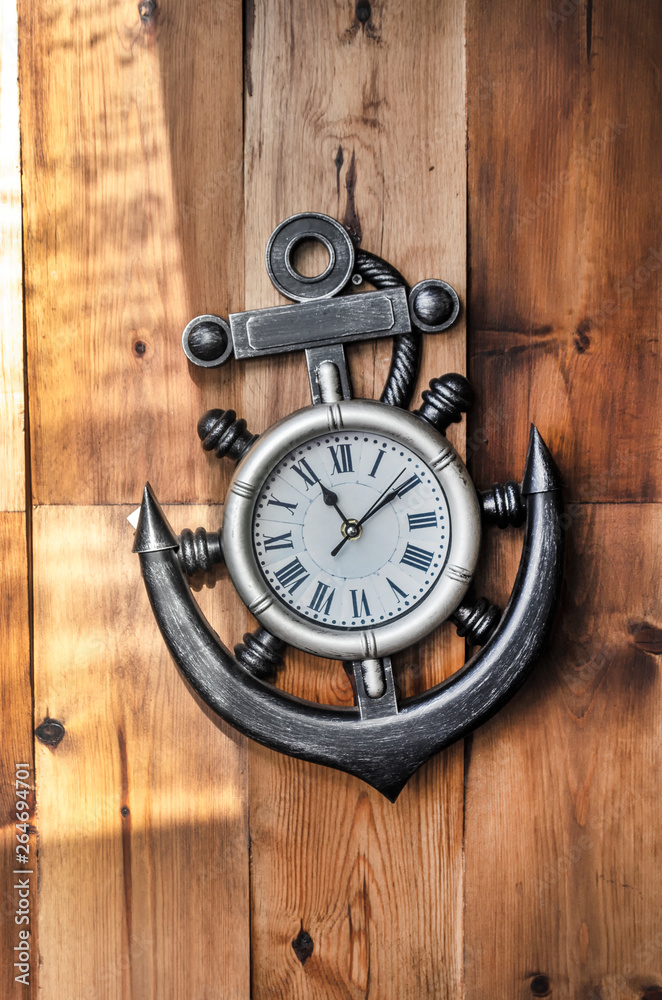 A nautical metal clock in the shape of an anchor on a wooden background showing the time. A nautical metal clock in the shape of an anchor on a wooden background showing the time.