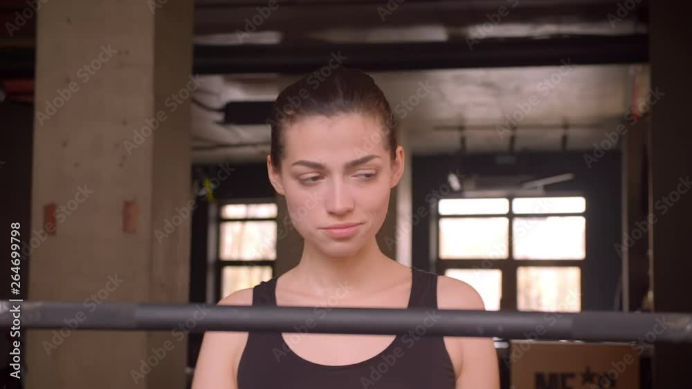 Closeup shoot of young attractive athlete female walking and getting ready to weightlifting in the gym indoors Closeup shoot of young attractive athlete female walking and getting ready to weightlifting in the gym indoors