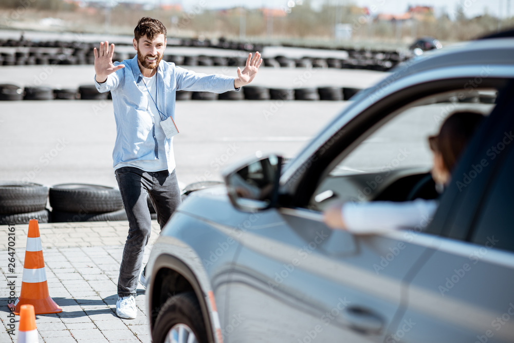 Male instructor showing stop with hands while teaching to park a car on the training ground at the school Male instructor showing stop with hands while teaching to park a car on the training ground at the school