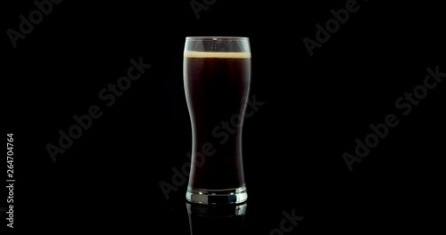 beer with foam is poured into a glass against a dark background