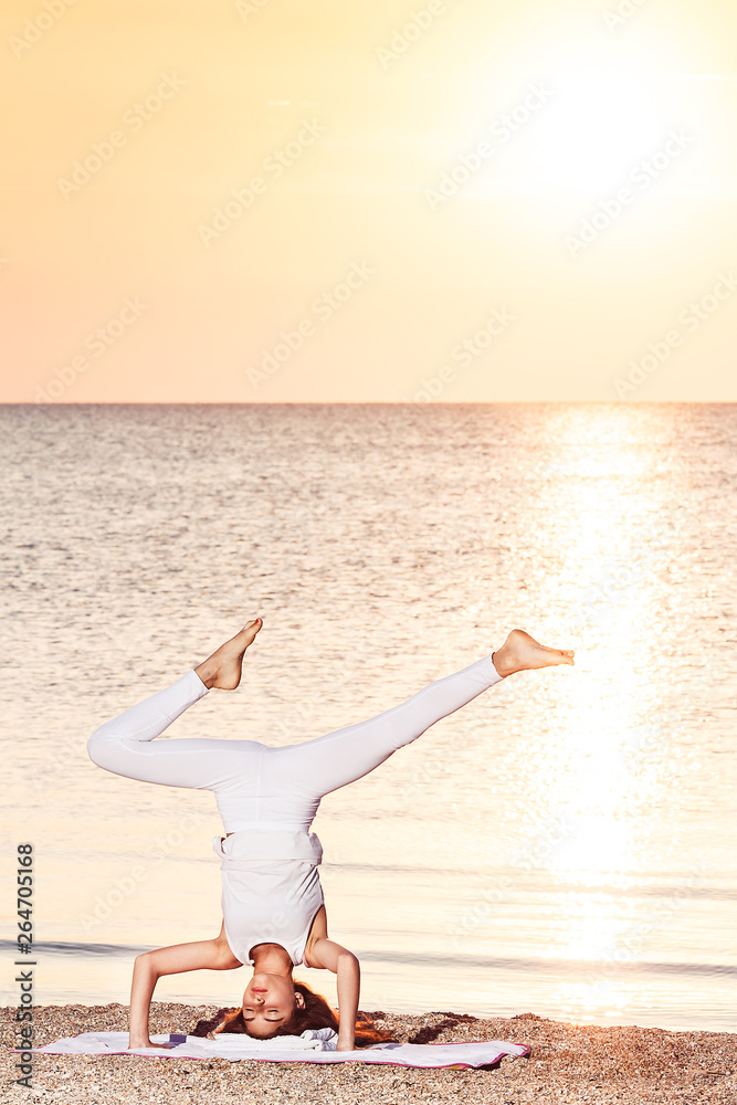 Obraz premium young girl doing yoga at sunrise on beach.