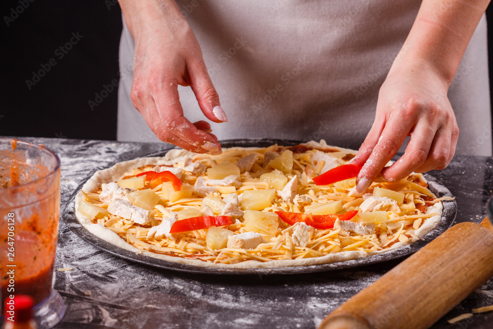 young woman in a gray aprons prepares a Hawaiian pizza