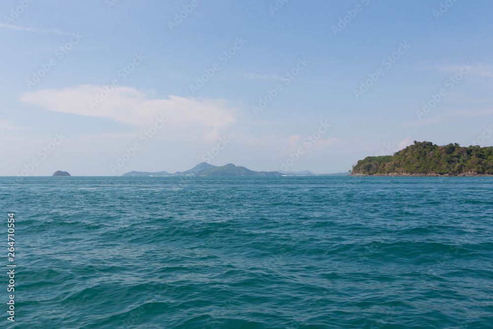 Blue sea and white sand with tropical mountains in the background Blue sea and white sand with tropical mountains in the background