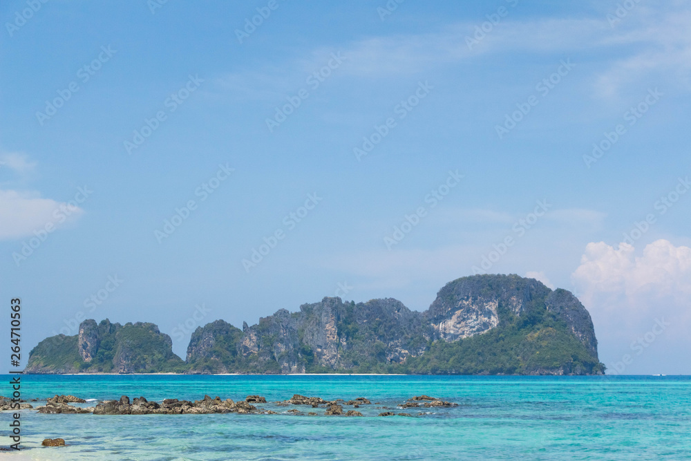 Blue sea and white sand with tropical mountains in the background