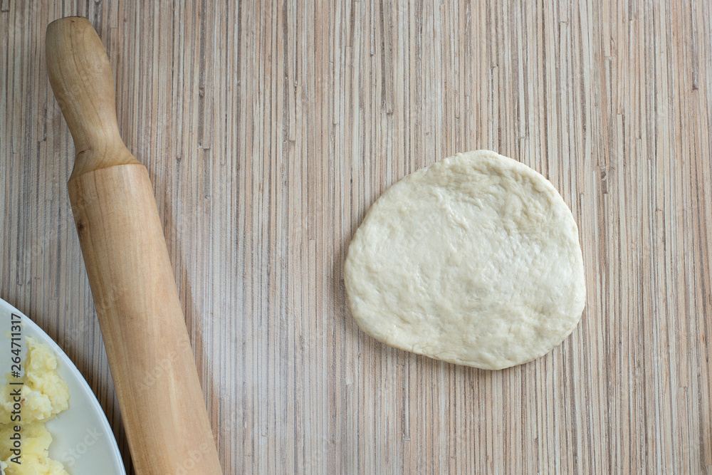 Yeast dough on the kitchen table is rolled out with a rolling pin for making a pie with a filling A cake of raw dough lies on the surface of the table for further preparation Yeast dough on the kitchen table is rolled out with a rolling pin for making a pie with a filling A cake of raw dough lies on the surface of the table for further preparation
