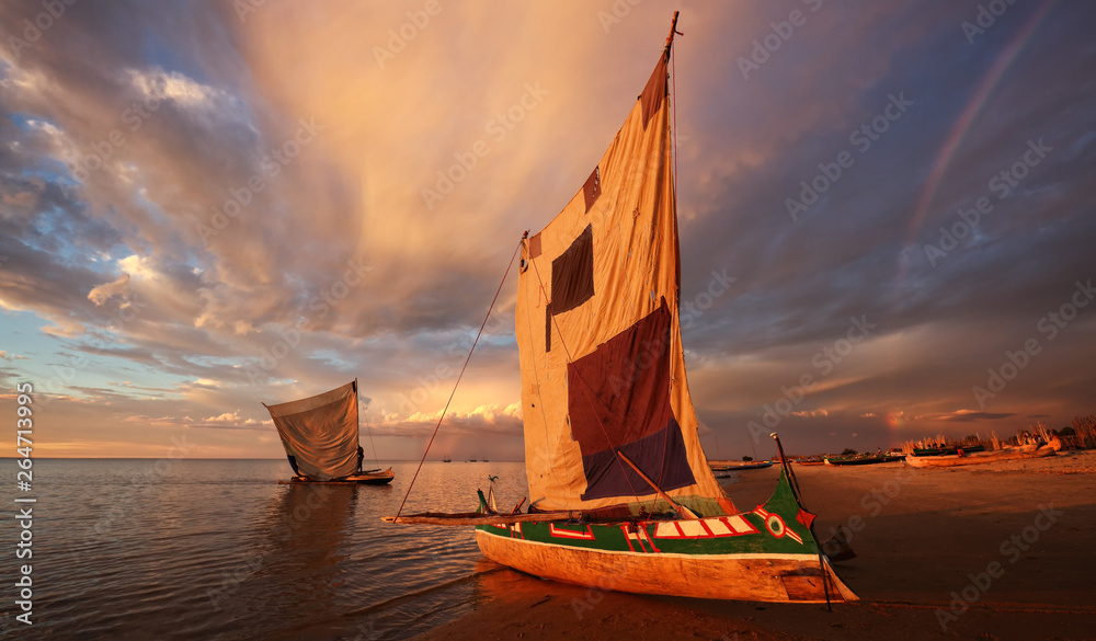 Traditional fishing pirogue at sunset with dramatic sky after a thunderstorm in Anakao, Madagascar - obrazy, fototapety, plakaty 