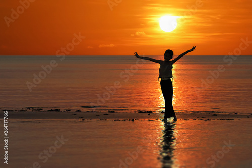 Silhouette of single Asian girl enjoying herself during sunset on the beach red sky