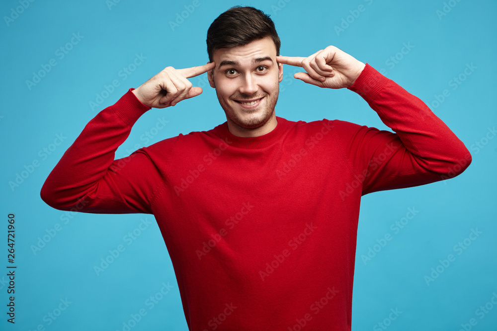 Horizontal portrait of attractive emotional young dark haired guy in red sweater holding fore fingers at his temples, saying: Are you insane? Bearded man rolling finger, mocking at crazy stupid idea Horizontal portrait of attractive emotional young dark haired guy in red sweater holding fore fingers at his temples, saying: Are you insane? Bearded man rolling finger, mocking at crazy stupid idea