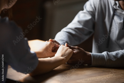 Close up hands diverse couple sitting at table holding hands