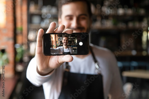 Fotografi Smiling restaurant owner holding smartphone with camera on make selfie