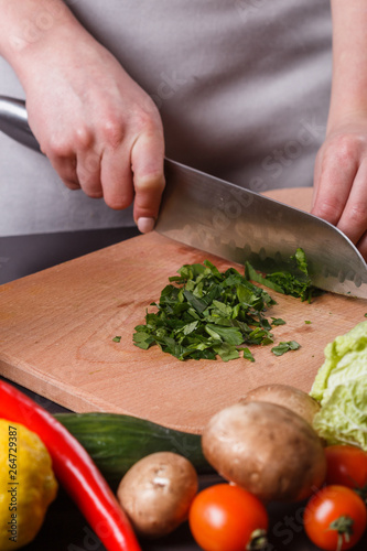 young woman slicing herbs in a gray apron