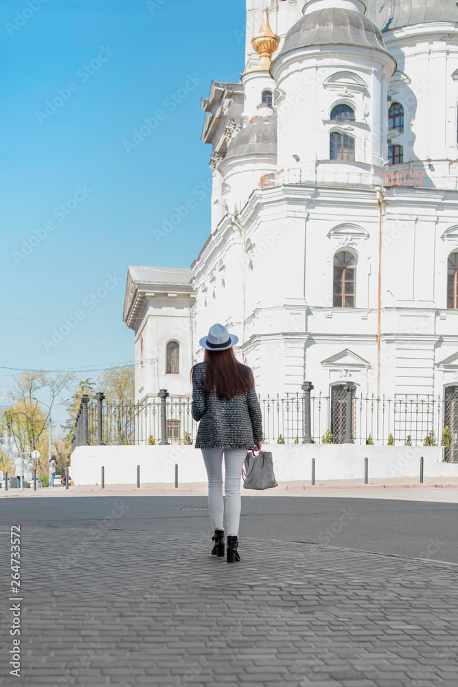 A girl stands on the street and looks at an Orthodox church.