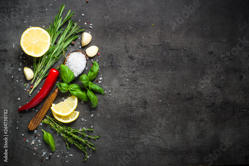 Selection of spices and herbs on dark stone table.