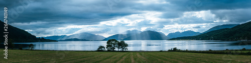 Mystic landscape lake scenery in Scotland: Cloudy sky, meadow, trees and lake with sunbeams, mountain range in the background. Loch Linnhe. photo