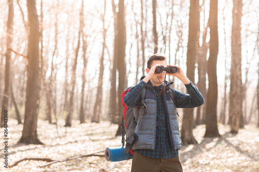 Young man with backpack looking at the binoculars, hiking in the forest Young man with backpack looking at the binoculars, hiking in the forest