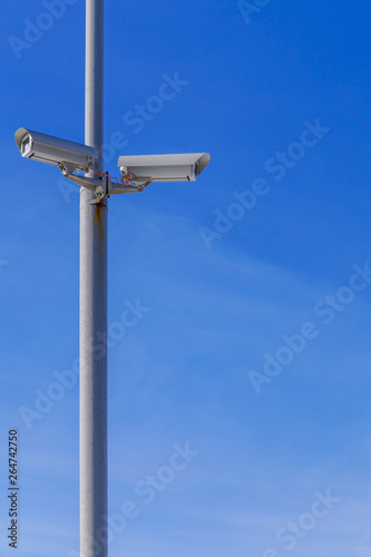 Two security cameras against the blue sky are monitoring.