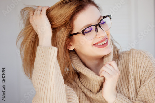Beautiful and stylish young woman in beige oversize sweater and glasses.