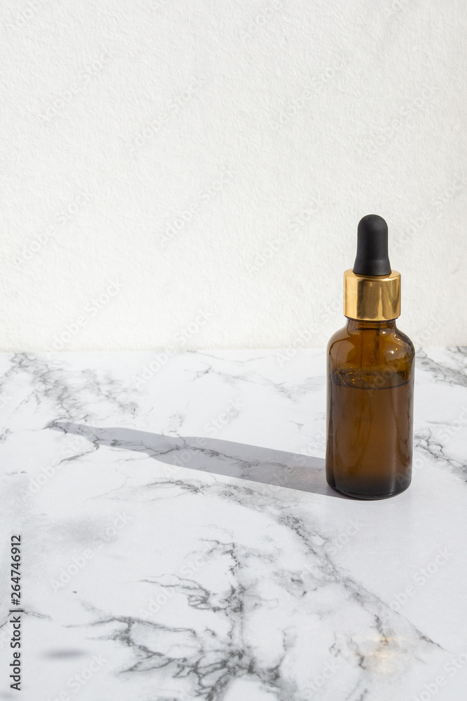 Pipette dropper with drop of natural oil above brown glass bottle on marble background. Natural organic skin care beauty products. Pipette dropper with drop of natural oil above brown glass bottle on marble background. Natural organic skin care beauty products.