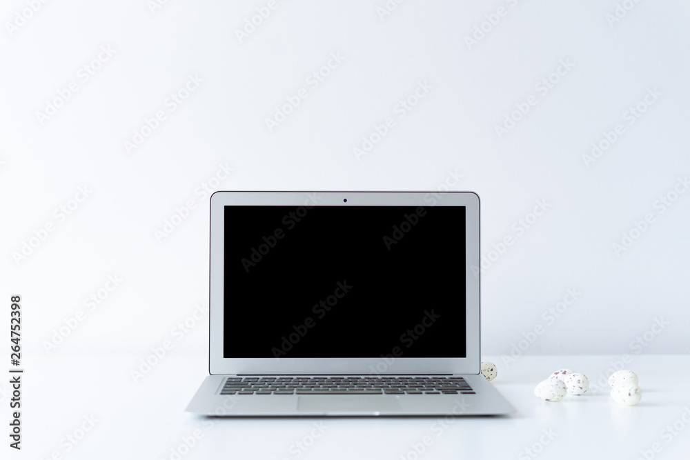 Open laptop and small easter eggs on the desk with white background Open laptop and small easter eggs on the desk with white background